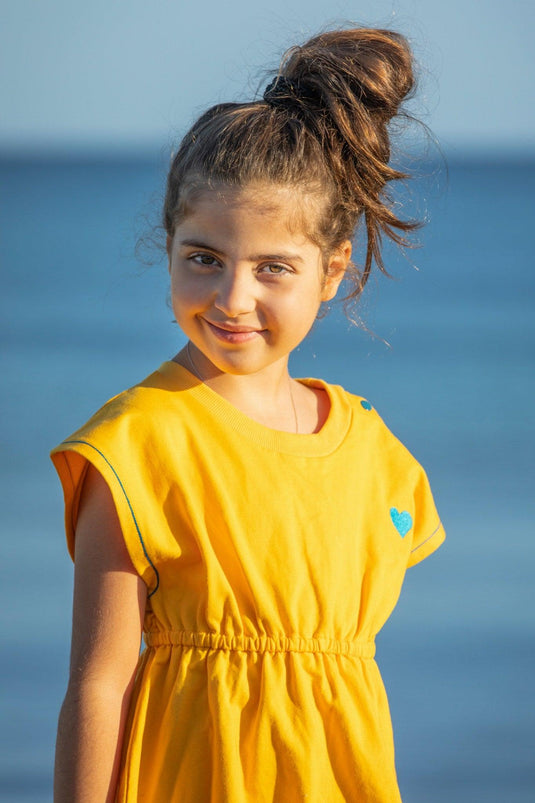 Small girl wearing the yellow retro dress with blue buttons in organic fabric by albaofdenmark