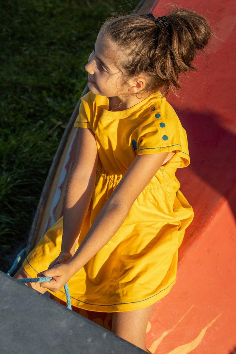 Load image into Gallery viewer, Girl wearing yellow retro dress with blue buttons in organic fabric by albaofdenmark
